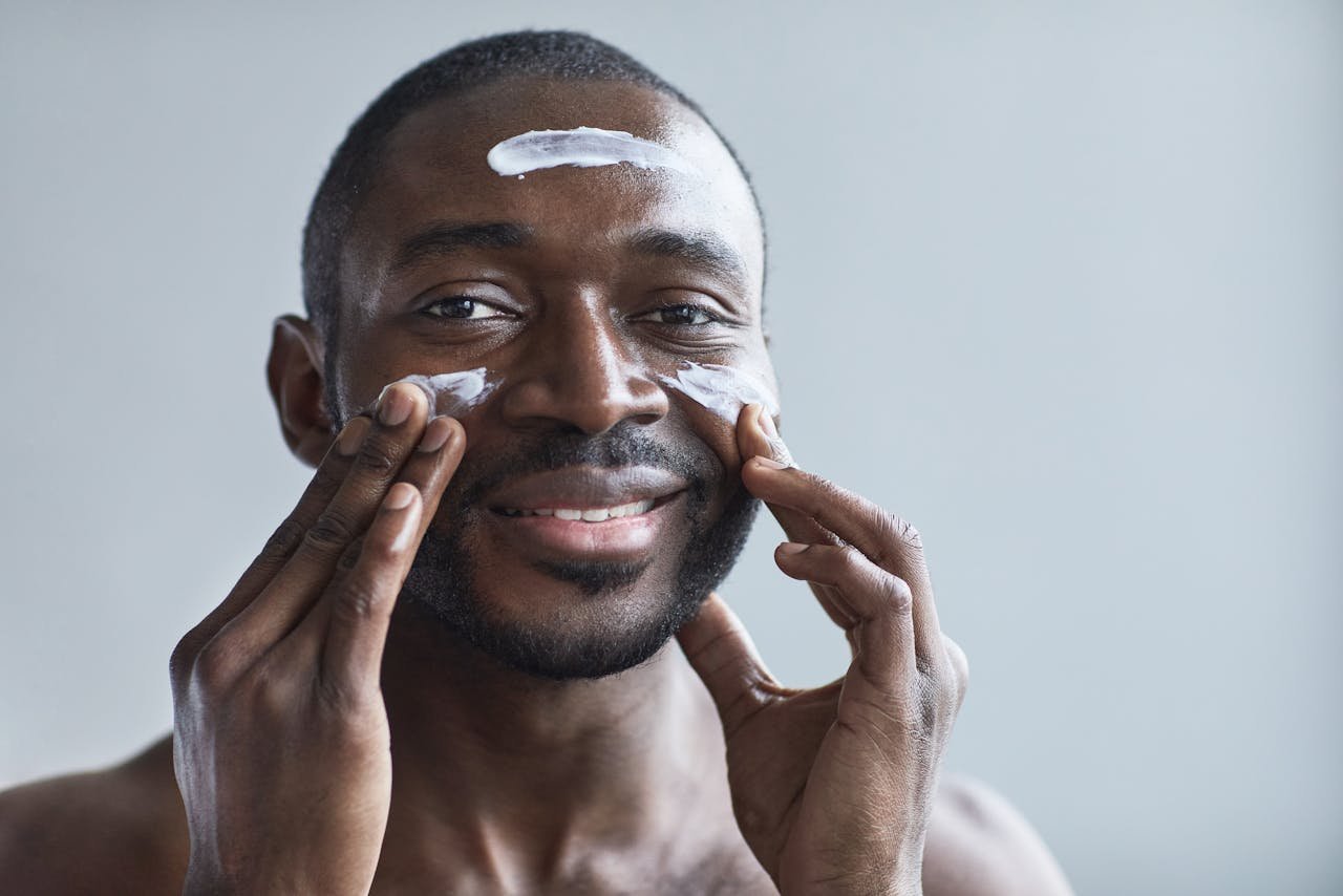 bedroom-bliss A cheerful African American man applying facial cream indoors.